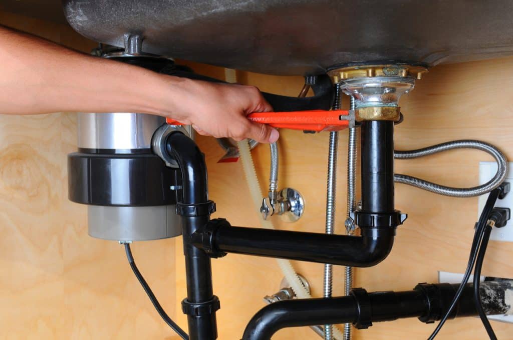 plumber using wrench beneath kitchen sink
